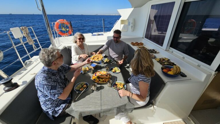 Quatre comensals asseguts a la banyera d’un catamarà davant de Barcelona, amb el brunch servit