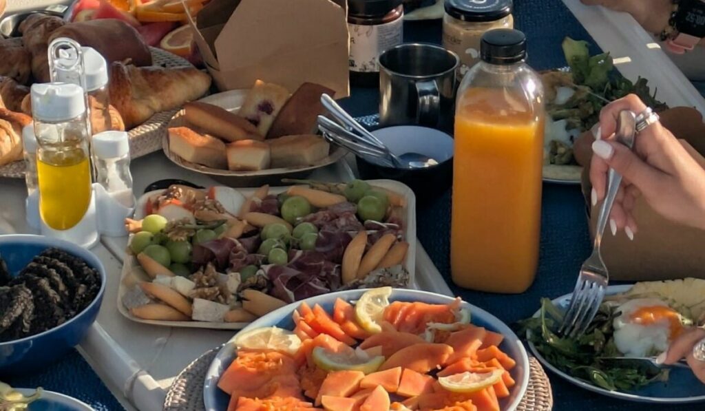 Table de brunch dressée sur le pont d’un catamaran à Barcelone : papaye, planche de charcuterie et fromages, viennoiseries, jus d’orange pressé