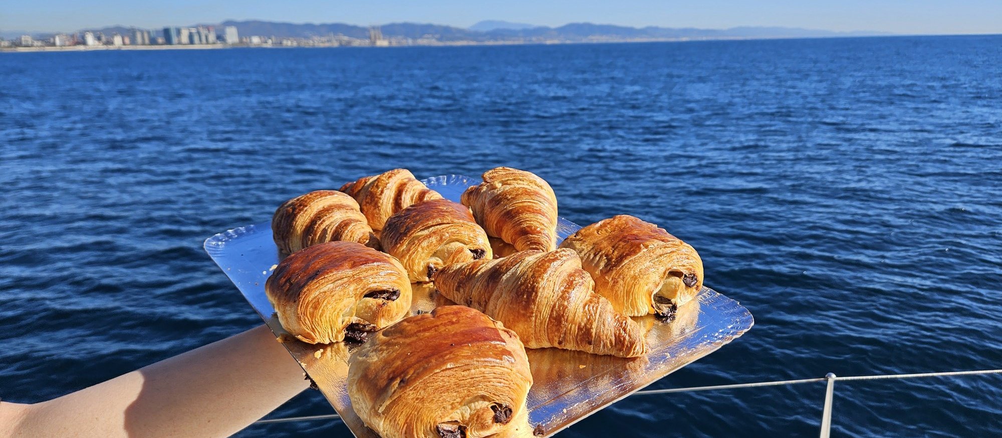 Plateau de viennoiseries tendu au-dessus de l'eau, skyline de Barcelone en arrière-plan