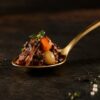 Beef bourguignon bite on a gold spoon, carrot and pearl onion